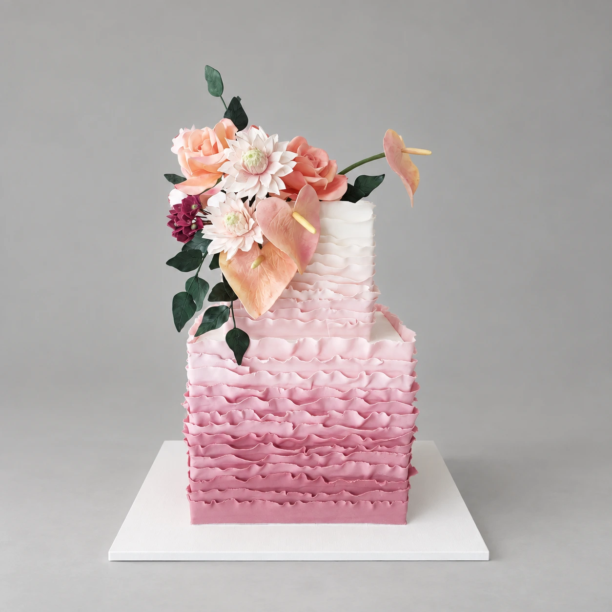 Two-tier square pink ruffle cake with peach and ivory flowers, burgundy accents and dark leaves