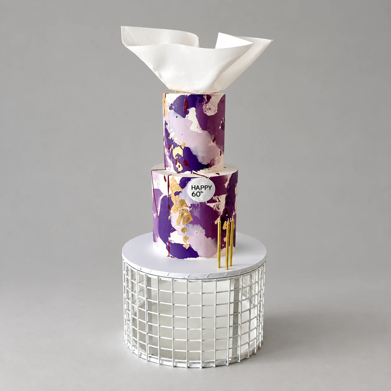 Two-tier purple and ivory cake with gold leaf, a white sculptural sail and birthday badge